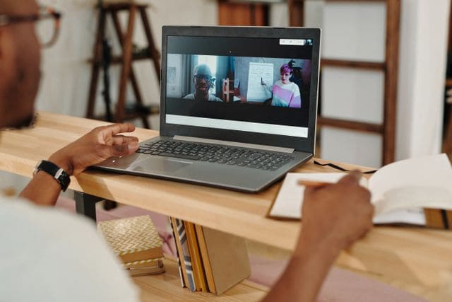 Mann macht sich während einer Videokonferenz am Laptop Notizen