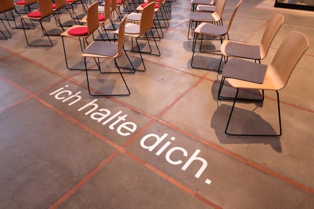 Motivationsbild für Deutschlerner: „Ich halte dich“ – Lernumgebung in einem Deutschkurs mit Stühlen und inspirierender Botschaft.